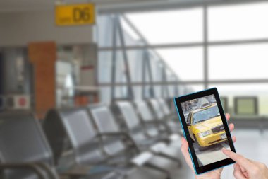 Sarı bir taksi tablet ekranıyla dokunmadan turist elleri. Kasıtlı olarak bulanık bir boş Havaalanı terminal içinde arka planda görüntüsüdür. Tüm potansiyel markalar kaldırılır.