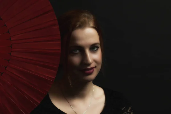 低关键的肖像诱人的年轻女子拿着红色风扇 都在黑暗的背景上 — 图库照片