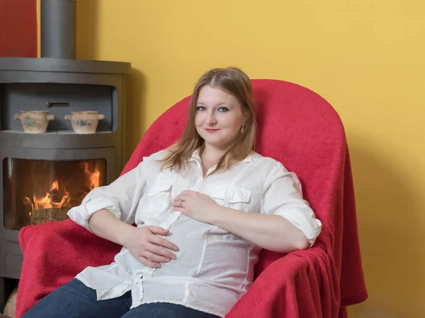 Gülümseyen Hamile Genç Kadın Rahatlatıcı Evde Soba Şömine Yanıyor Sandalyede — Stok fotoğraf