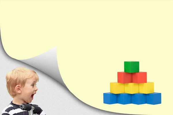 Surprised blond boy is looking at a pyramid of wooden cubes — Stock Photo, Image