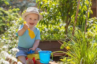 Gülümseyen çocuk bahçede plastik tırmıklar tutuyor.