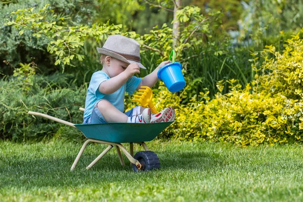 Netter Kleiner Junge Mit Hut Sitzt Auf Einer Grünen Schubkarre — Stockfoto