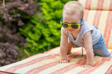 Güneş gözlüğü takan küçük bebek bahçede iskemlede emekliyor..