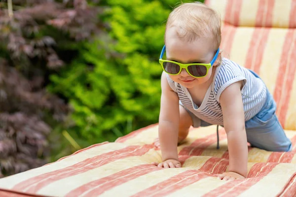Güneş gözlüğü takan küçük bebek bahçede iskemlede emekliyor..