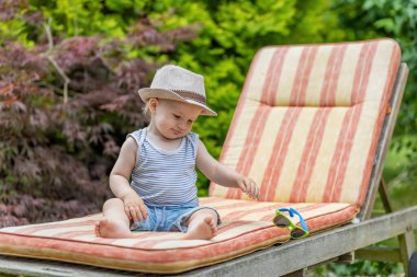 Bebek, bahçedeki iskemlede oturan güneş gözlüğünü atıyor..