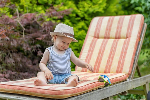 Bebek, bahçedeki iskemlede oturan güneş gözlüğünü atıyor..