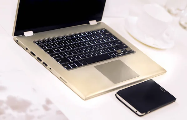 Laptop ile cep telefonu ve tabloda çay bardağı. Görünümü kapatın.