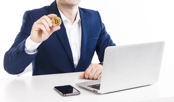 Dizüstü bilgisayar ve telefon ile masada beyaz arka plan üzerinde çalışırken altın bitcoin tutan bir iş adamı. Portre.