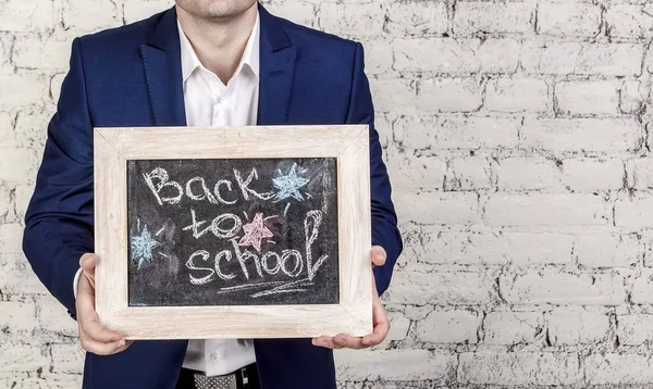 Man in classic suit holds blackboard with title Back to school. White bricks background. No face, horizontal banner, copy space. Start of school year concept.