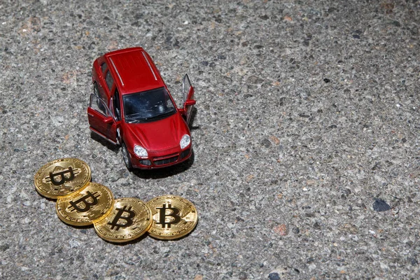 Bir boşaltmak asfalt doku zemin üzerine kırmızı lüks crossover araba closeup yakınındaki dört altın bitcoin para. Finans cryptocurrency kavramı.
