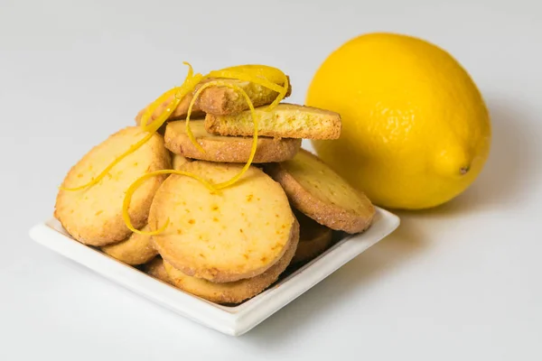 Galletas de limón caseras en un platillo blanco cerca de limón fresco sobre fondo blanco. Primer plano, aislado — Foto de Stock