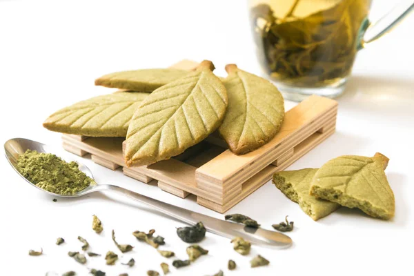 Ev yapımı matcha yeşil çay kurabiye kurabiye şeklinde yeşil çay yaprakları yeşil çay bardağı beyaz arka plan üzerinde izole yakınındaki ahşap stand.
