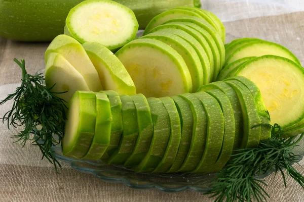 Slices of sliced zucchini for future use in a recipe with green dill on a glass plate.