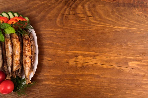 Capelin, altın kahverengi oluncaya kadar yağda kızartılmış bütün domates ile bir tabakta koydu ve dilimlenmiş salatalık ve biber.