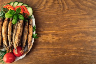 Kızarmış deniz balık tabakta domates, dilimlenmiş biber, salatalık, taze fesleğen yaprakları, maydanoz ve dereotu.