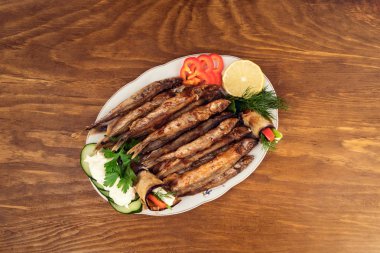 Kızarmış patlıcan ile dilim salatalık, tatlı biber, limon dilim, dereotu ve maydanoz doldurulmuş capelin yağda sebzeler ile balık yemek.