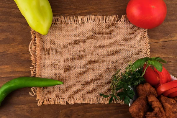 Linen fabric on a wooden background, in the corners of the whole fruit of sweet pepper, bitter pepper, tomato and a plate with pieces of fish in batter, deep-fried, making a recipe.