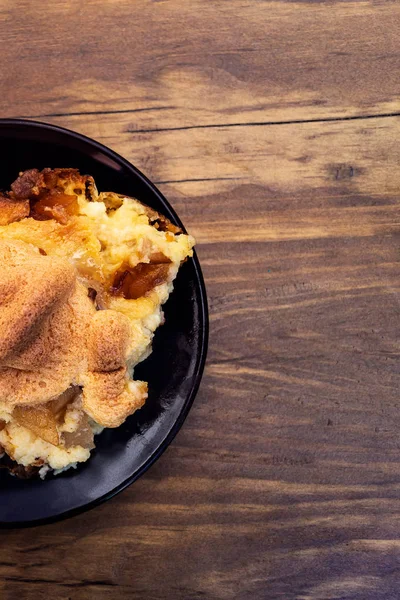 Homemade casserole with apples, cottage cheese and cheese, laid on a round plate on a wooden background, top view.