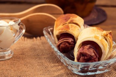 Puf böreği, peçeteye keten, ahşap mutfak maşa, ekşi krema sos tekne içinde yapılmış bir cam levha altın bir kabuk ile fırında pişmiş sarılmış et sosis.