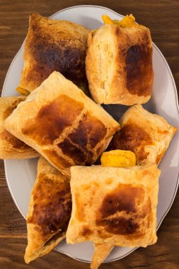 Puf böreği rulo dolması yumuşak peynir, altın kahverengi oluncaya kadar fırında pişmiş bir tabak içinde yığılmış, top ahşap arka plan üzerinde görünümü.