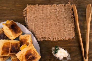 Fırında pişmiş peynirli puf çörekler ahşap zemin, mutfak maşa, yanında bir tabak içinde keten peçete, ekşi krema sos tekneyle dereotu, üstten görünüm bir delikanlı ile yığılmış.