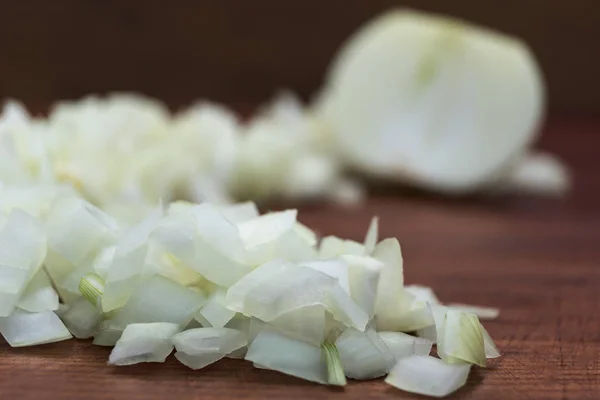 The onion cut into small pieces, laid on a wooden background together with a half of the cut bulb.