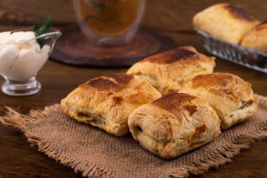 Doldurma bir keten kumaş peçete, ekşi krema ile et suyu tekne, tüm ahşap arka plan üzerinde bir bardak limonlu çay peynirli puf böreği çörek.
