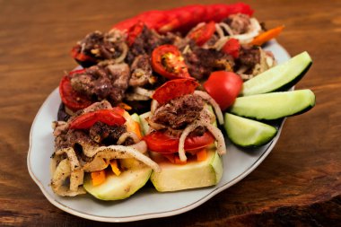 Bir tabak pişmiş kabak ve patlıcan, üzerine soğan ve domates ile kızarmış et katmanları koyulur.