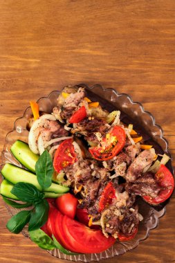 Pişmiş sebze ile et ızgara ve dilimlenmiş taze domates, salatalık ve fesleğen yaprakları, dikey çerçeve, ahşap arka plan.