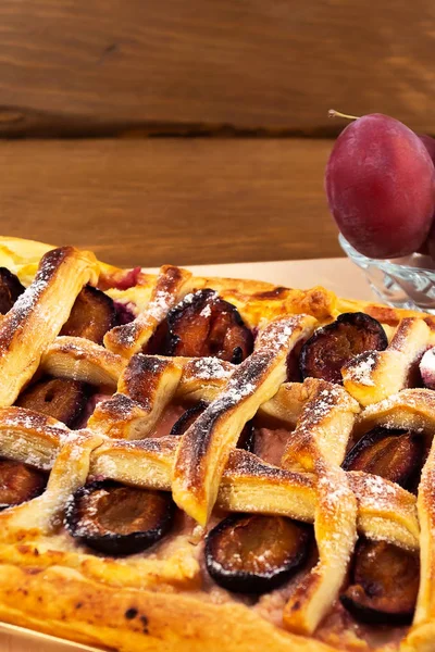 Puff pastry cake with baked plums in the cells, vertical frame, wooden background.