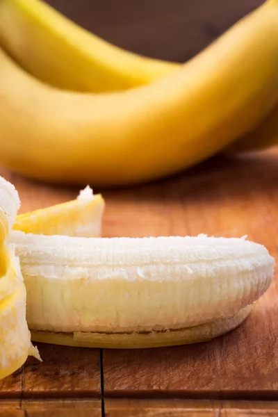 Ripe bananas with yellow peel and white pulp on wooden background.