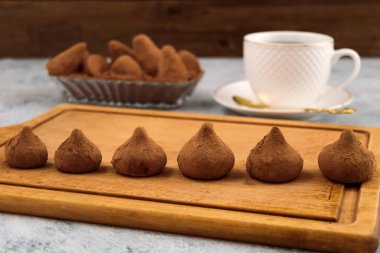 Çikolata truffles ahşap bir masa, bir satırda bir beyaz kupa çay için fincan tabağı ile kaplı.