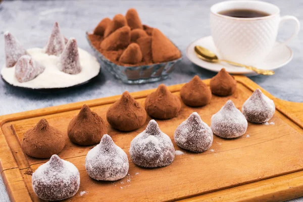 Chocolate truffles in powdered sugar and cocoa powder on a wooden Board, white Cup with tea.