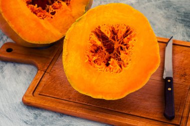 Olgun kabak portakal bir orta ile kesilmiş iki parçaya bir ahşap tahta üzerinde bir bıçak.