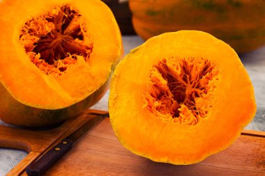 İki bölümden olgun kabak, turuncu hamuru ve çekirdek, ahşap mutfak kurulu bir bıçak lif halinde kesilmiş.