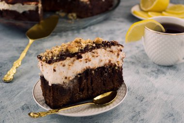 Çikolatalı kek parçası. Beyaz krem tabakası. Ceviz ile serpilir. Fincan çay ve limon. Tatlı yemekleri.