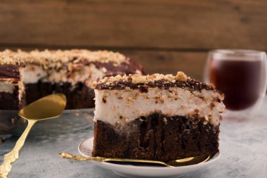 Bir plaka üzerinde çikolatalı kek parçası. Beyaz ve kahverengi tabaka. Ezilmiş ceviz. Kaşık ve tatlı spatula. Ahşap arka plan.