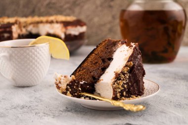 Bir plaka üzerinde çikolatalı kek parçası. Tatlı yeme. Bir dilim limon Kupası kenarında. Bitkisel çay sürahi.