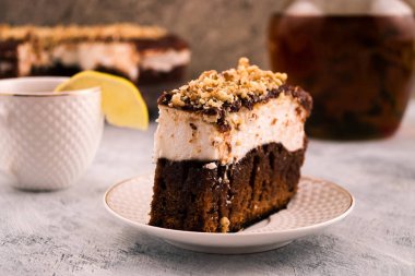 Çikolatalı kek parçası. Krem beyaz bir tabaka. Rendelenmiş ceviz Sprinkles. Limon Kupası kenarında. İçki sürahi. Açık renkli.