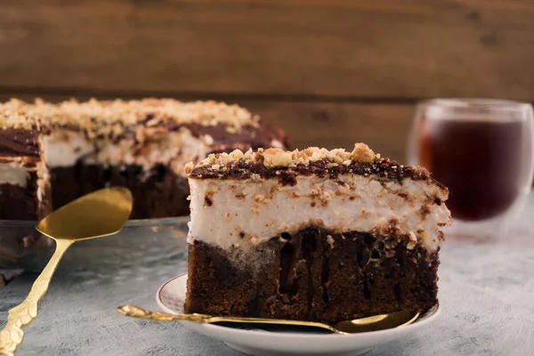 Bir plaka üzerinde çikolatalı kek parçası. Beyaz ve kahverengi tabaka. Ezilmiş ceviz. Kaşık ve tatlı spatula. Ahşap arka plan.