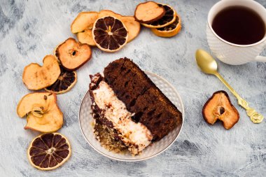 Çikolatalı kek bir plaka üzerinde. Beyaz beze, kahverengi hamur. Kurutulmuş meyve dilimleri. Beyaz kupa çay ile. Açık renkli.