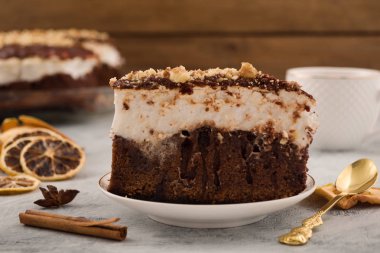 Bir parça çikolata kremalı pasta. Kabuk tarçın, kurutulmuş limon dilimleri. Metal çay kaşığı. Açık renkli.