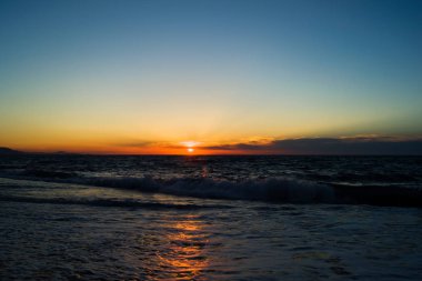 Batan güneşin denizde ufuk üzerinde. Güneş ışığı su yansıması. Küçük dalgalar köpük ile.