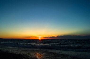 Parlak ve güzel günbatımı denizde. Güneş ışınları, bulutların arasından onların yol yapmak. Küçük bulutlar ufukta. Saf mavi gökyüzü. Güneş ışığı su yansıması.