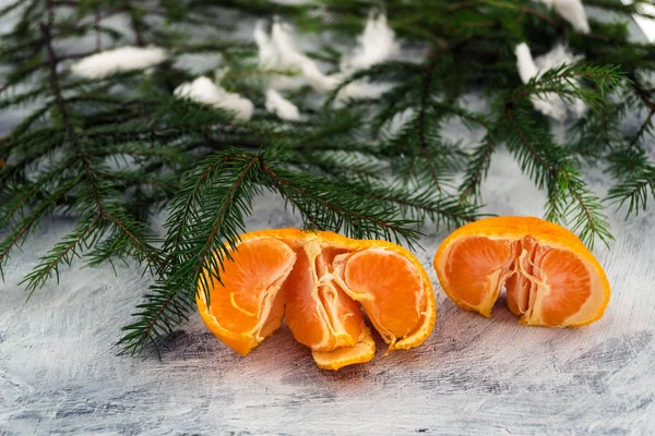 Ripe mandarins broken into slices. Orange slices on a light background. Green branches ate under the snow.