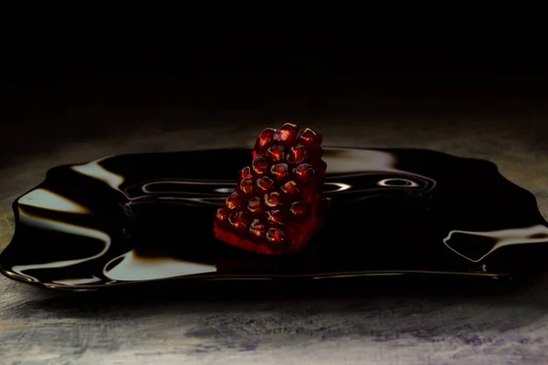 Olgun nar siyah bir plaka üzerinde. Tropikal meyve. Cam yansıması. Sulu kırmızı tahıl.