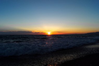 Akşam deniz manzarası. Sudaki yansıması ile gün batımı. Kum sahil şeridine.
