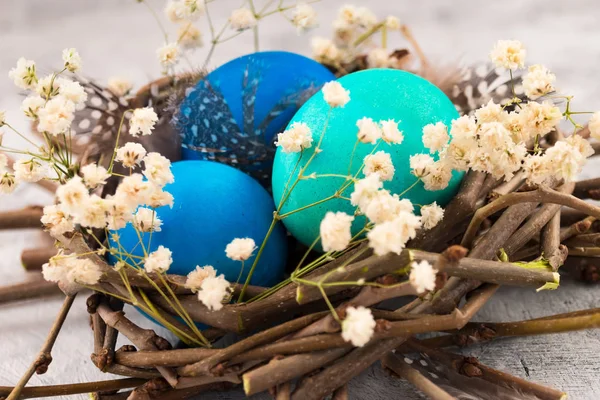Kuş yuvası beyaz çiçekler ve tüyler yeşil ve mavi Paskalya yumurta. Dekorasyon için hafif bir arka plan üstünde Paskalya yortusu.