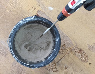 Adam matkap karıştırıcı elinde tutuyor. Adam gri beton ve baş kova içinde karıştırma.