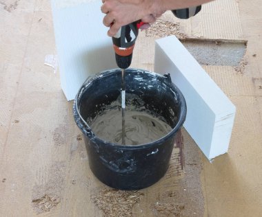 Adam matkap karıştırıcı elinde tutuyor. Adam gri beton ve baş kova içinde karıştırma.